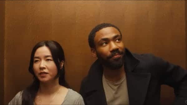 Glover and Esrkine standing next to each other in an elevator as they both look away from each other.